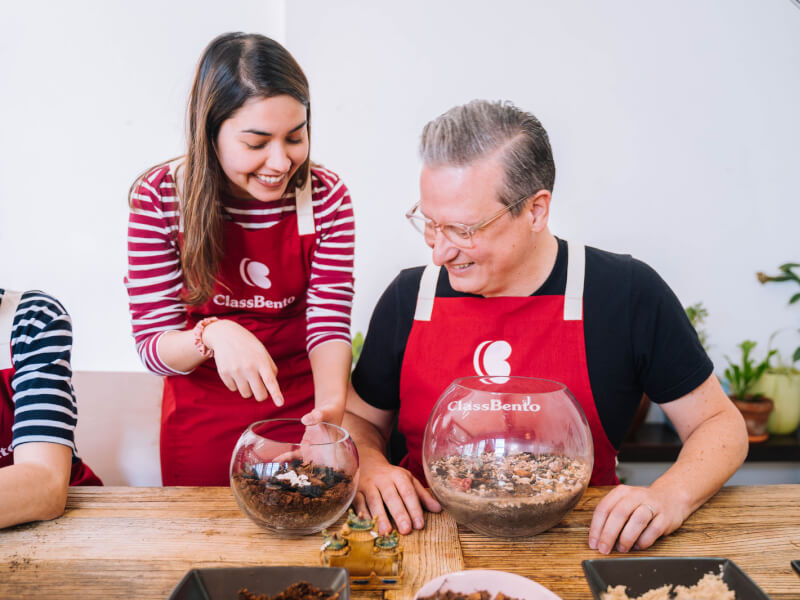 A woman and man are making glass terrariums at a wooden table